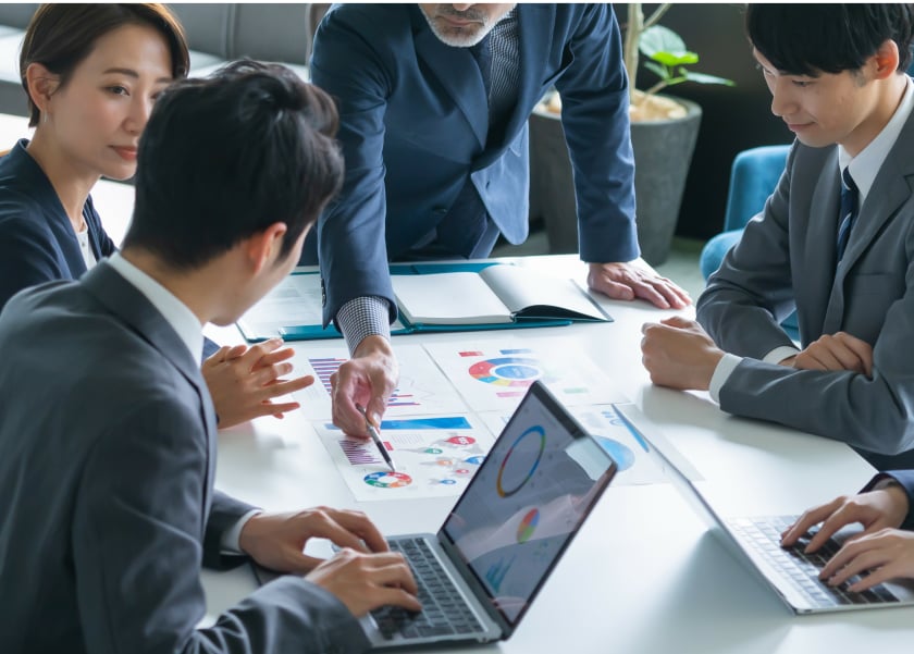 異なる事業部の社員が資料を参考にしながら会議をしているイメージ