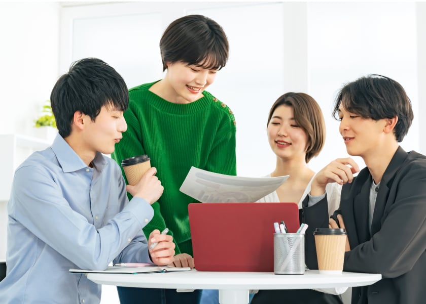 資料を見せながら立って話す一人の社員と、座ってそれを覗き込む3人の社員のイメージ